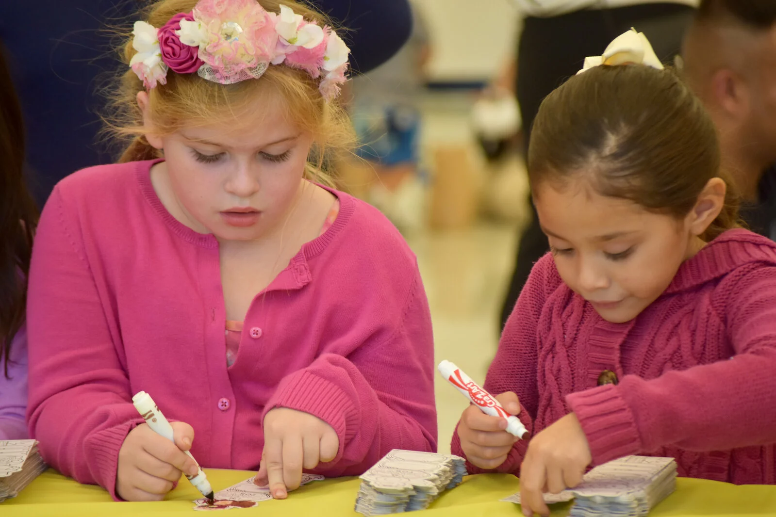 Two students in pink sweaters coloring bookmarks
