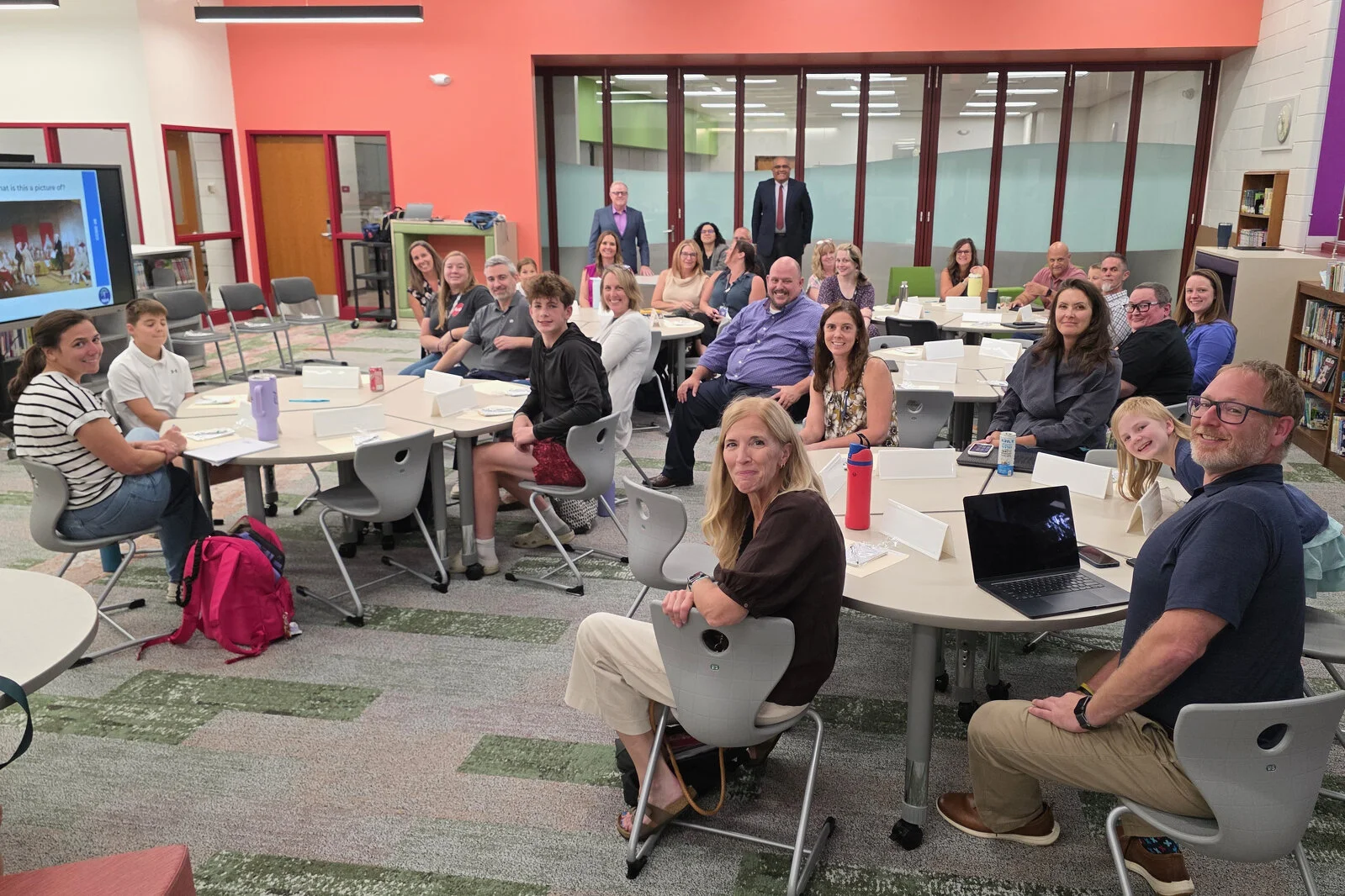 Members of the Portrait of a Learner team looking at the camera for a group photo while seated at their tables